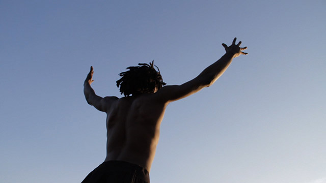 a single male dancer looking up and throwing his arms up at a blue sky