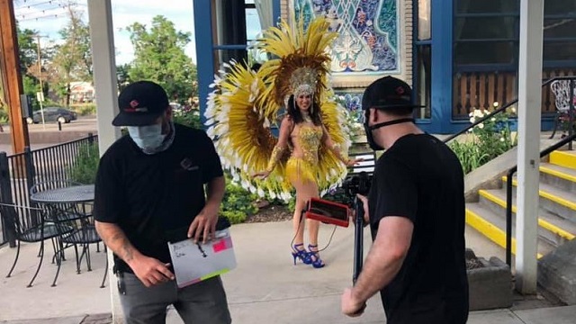 a samba dancer in full costume waits in front of a film crew to begin dancing