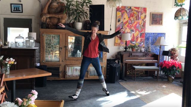 a lean, light skinned woman dances in a living room filled with antique furniture