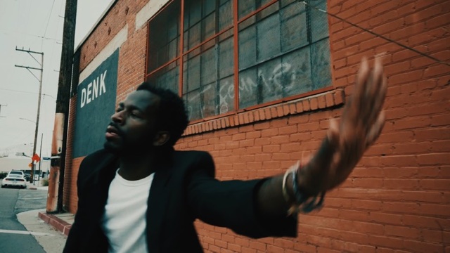 a single male dancer in front of a brick wall, throwing his hand to the side with eyes closed