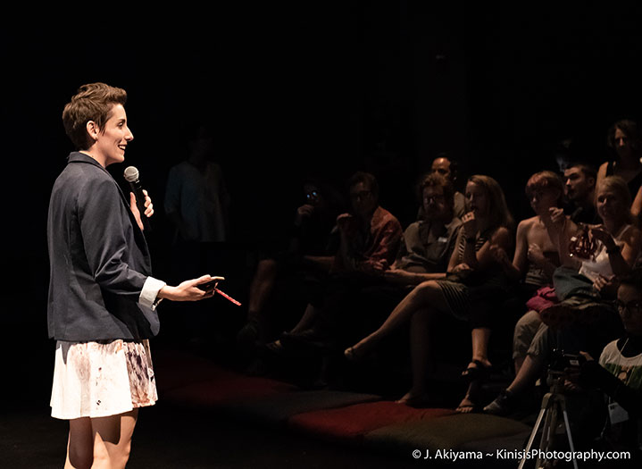 Sans Souci Festival Director Michelle Bernier greeting the audience at our 2018 Premiere, speaking into a microphone and holding a red vine candy