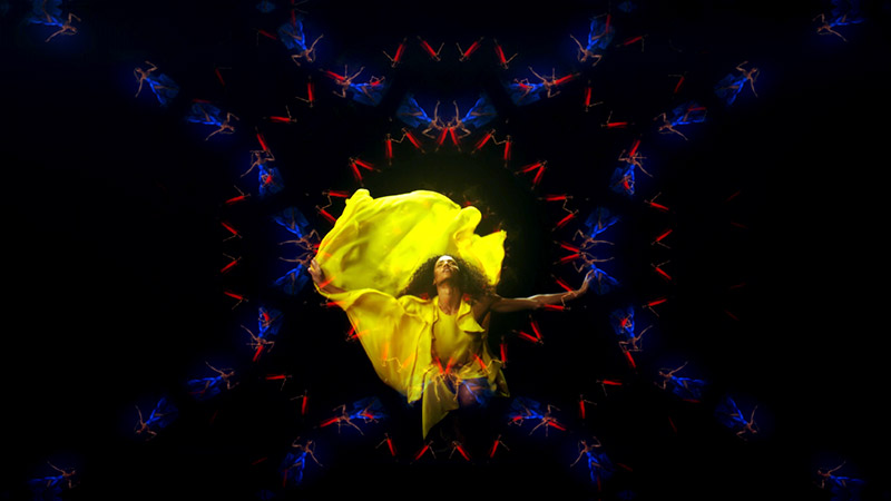 a dancer in yellow flowy fabric explodes with energy, on a kaleidoscope background of other dancers in blue and red concentric circles