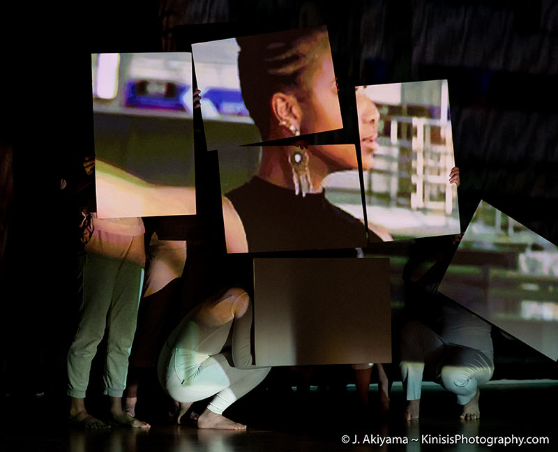 several live dancers are holding white squares, upon which is projected the image of another dancer