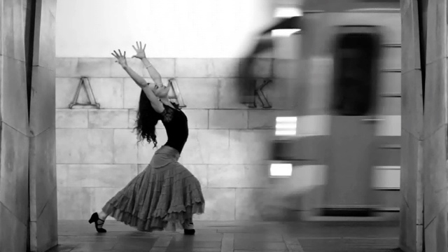 a female flamenco dancer extends her arms with closed eyes, just as a subway train arrives