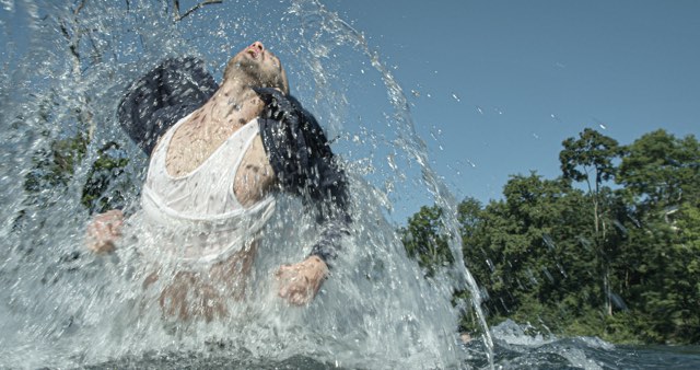 a light skinned male dancer jumps out of splashing water