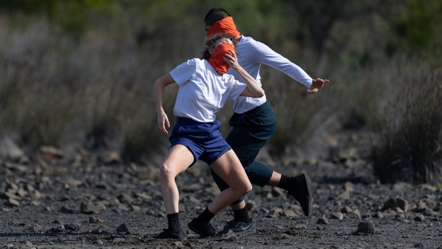 two dancers in casual clothes and orange masks in angular shapes on a rocky surface