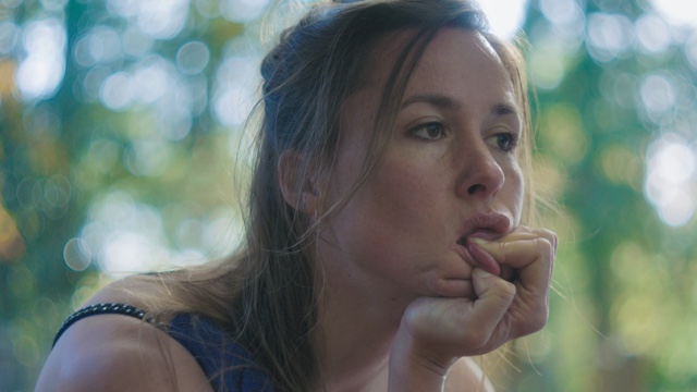 a light-skinned woman with messy hair pulls on her mouth and stares