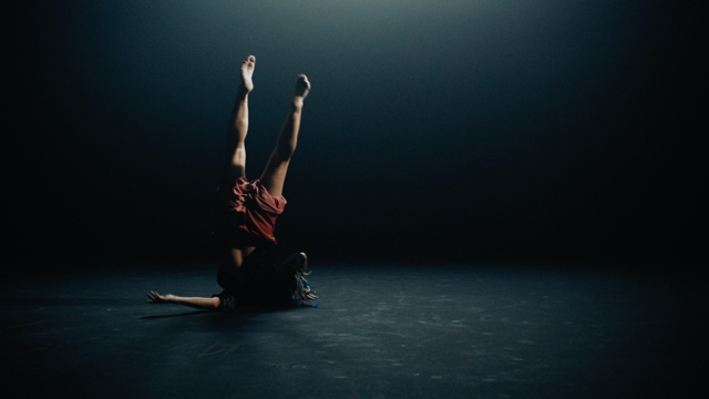 a dancer balances precariously on her shoulder, with her feet toward the sky