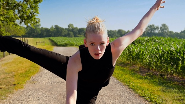 a light skinned dancer with blonde hair stares at the camera with arm and leg outstretched