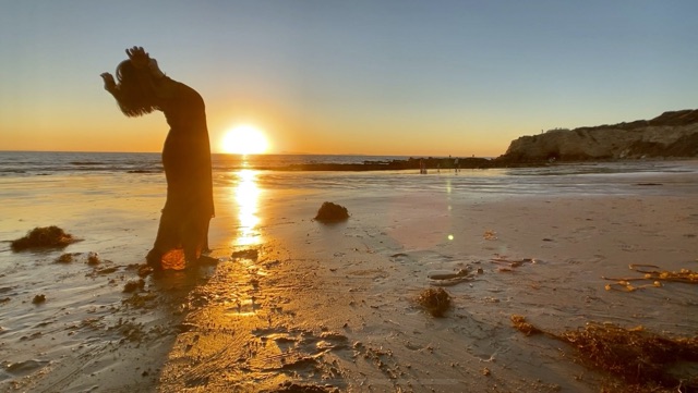 a dancer on the beach at sunset raises her chest to the sky