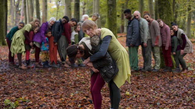 an older woman hugs a young girl in the foreground, several dancers lean on one another in the background