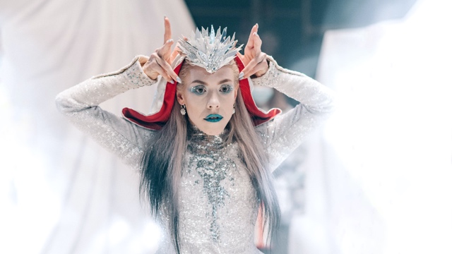 a dancer in an elaborate sparkling dress and crown wearing green lipstick