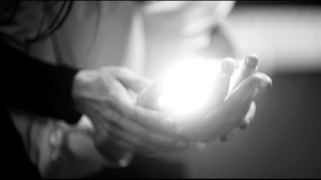 two pairs of light skinned hands cupping a ball of light