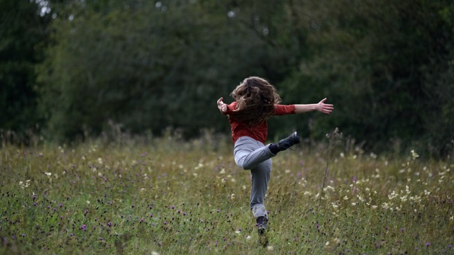 a dancer with jeans and boots leaps through a flowery meadow