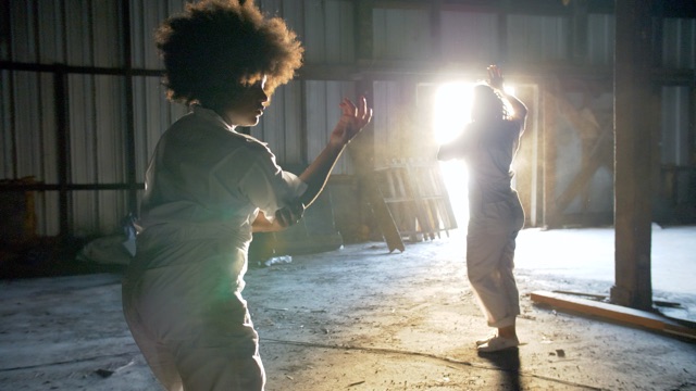 two women dancers in white jump suits in an abandoned factory, framed by a bright window