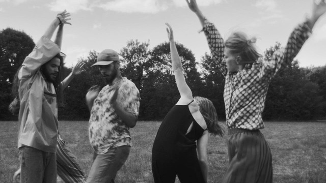 four dancers in a field in black and white fling limbs wildly