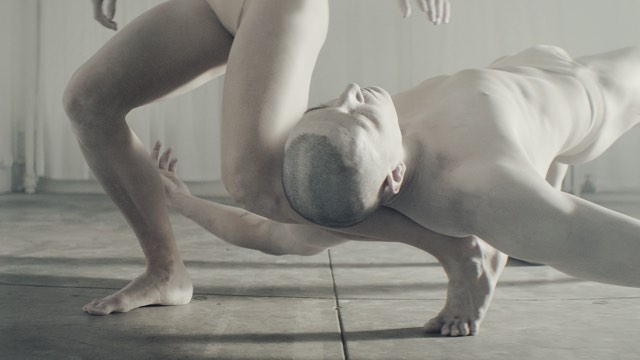 two white-paint-covered dancers, one resting his head on the other's ankle