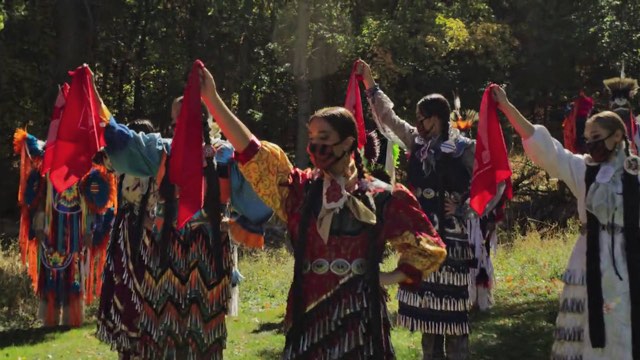 several Native American dancers raise a hand holding a red flag