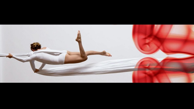 an aerial dancer suspended from a fabric sideways, with red misty clouds below