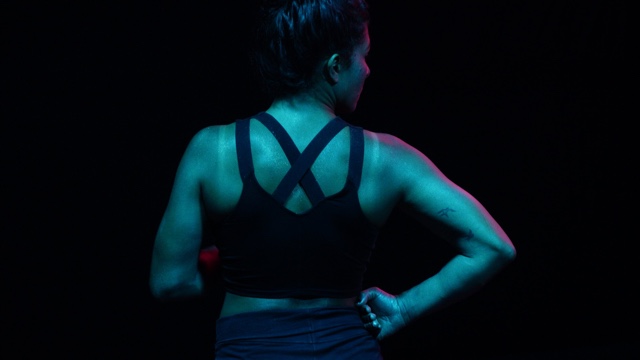 a woman's muscular back is washed with a pink light from the side