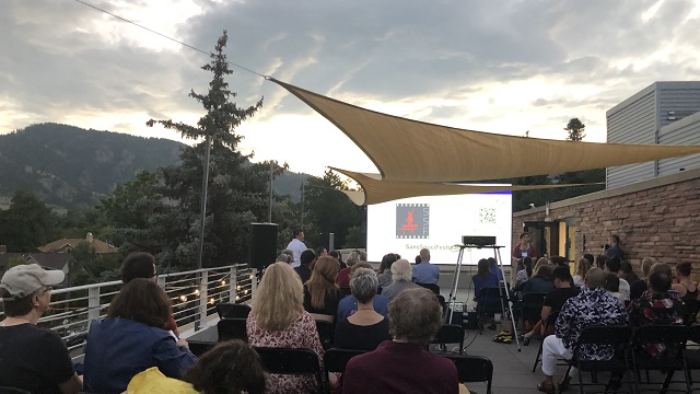 many people seated facing a projector screen with the SSF logo on it and the mountains of Boulder, Colorado in the background
