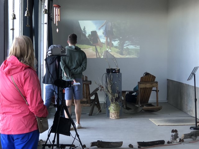 four people, including one in a rocking chair, watch a dance film projected onto a concrete wall