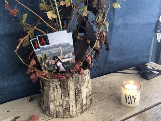 dried flowers in a distressed wood pot holding San Souci fliers next to a candle with the word HOPE printed on it