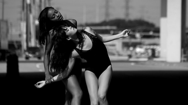 two women - one dark skinned and one light skinned - dance under an overpass in Dallas