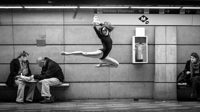 a ballet dancer leaps acrobatically at a subway stop while other passengers go about their business