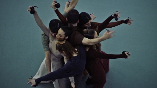 a group of dances clusters together tightly with arms outstretched