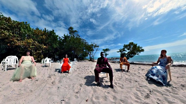 five people in colorful suits and dresses sit in plastic chairs on a sandy beach