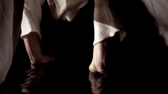 a closeup of a dancer's two wrists as their palms make contact with a dark, wet surface