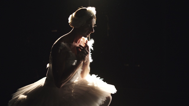 a dancer in a feathery dress looks pensively at the floor