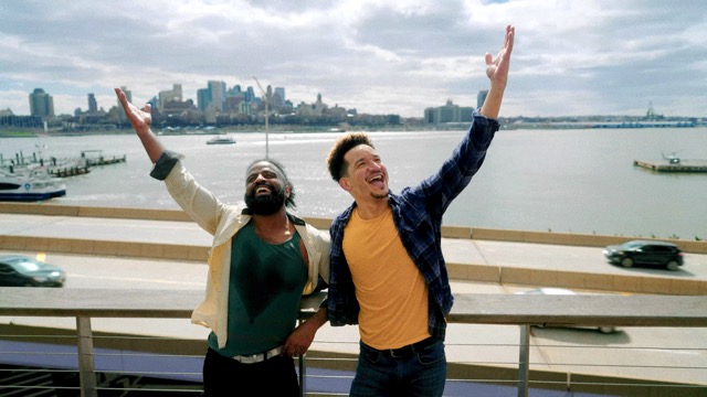 two dancers embrace and lift an arm, with a backdrop of NYC