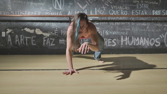 a woman with a blue streak in her hair looks into the camera while squatting low to the ground