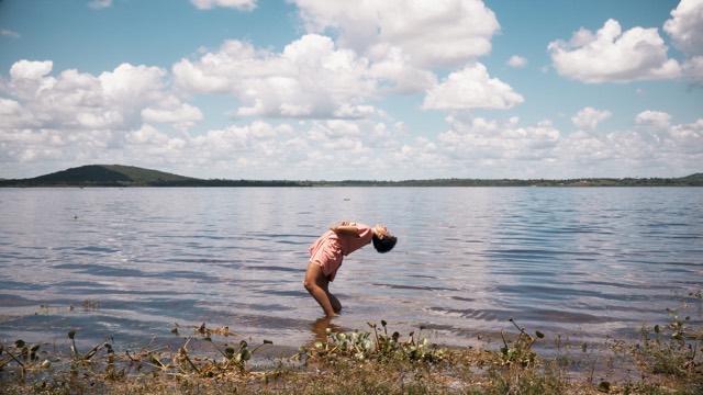 a person in a pink dress does a deep back bend while standing in a shallow lake