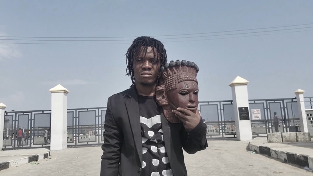 a man looks into the camera intensely while he holds an intricate clay sculpture of a face