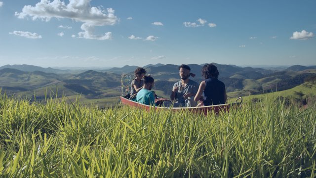 four people, one blindfolded, sit in a small boat placed atop a hill among a series of many other hills