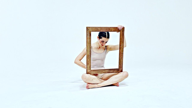 a dancer sits cross-legged holding a wooden frame in her lap