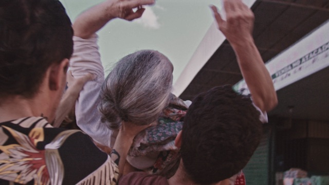 several dark haired people carry an older person above their heads