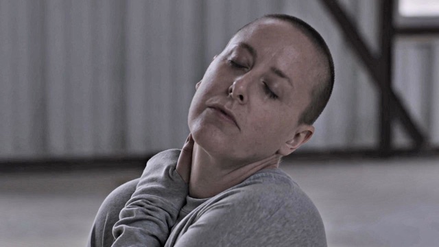 a woman with close shaved hair gives an expressionless look with eyes closed and head tilted