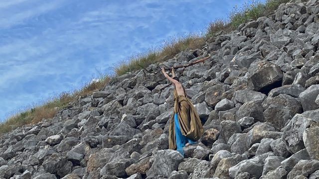 a man wields a tree branch over his head while standing in a field of boulders