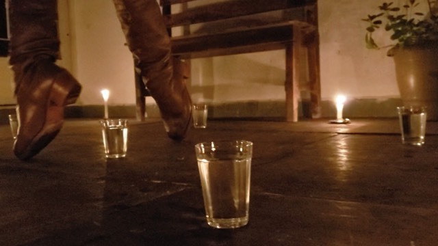 booted feet stand on their toes amid five glasses of water placed on the ground