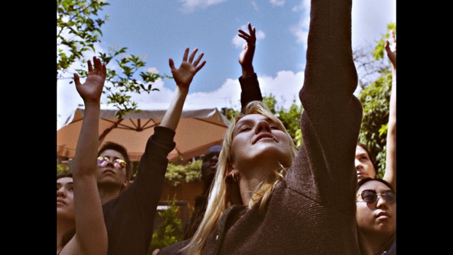 several young people look skyward, left arms raised tall