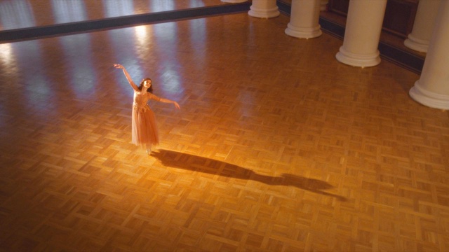 a ballerina en pointe with arms extended in a diagonal in a large ballroom