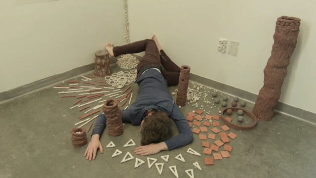 a dancer lies face down, surrounded by small ceramic and clay art objects