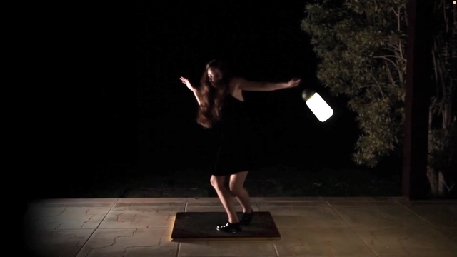 a woman dancing on a small platform with a dark background, holding a lantern