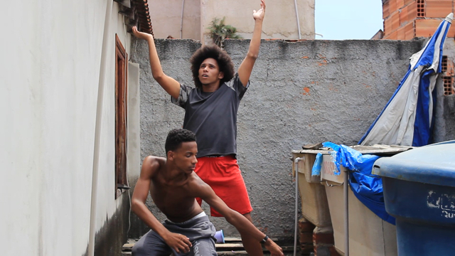 two young men dance in a small enclosed area behind a building