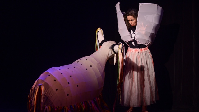 a woman stares intently at an animal made of fabric and ribbons