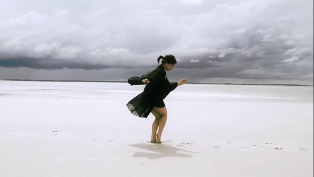 a woman in a black dress plants her feet in white sand with storm clouds behind her